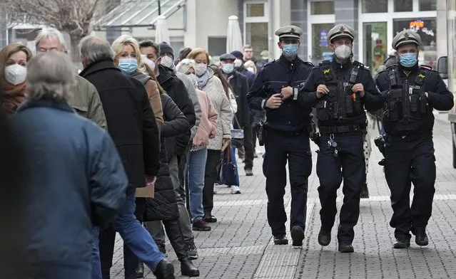 Police officers walk past people who queue in front of a vaccination center to get vaccinated against the coronavirus in Duesseldorf, Germany, Monday, December 6, 2021. (Photo by Martin Meissner/AP Photo)