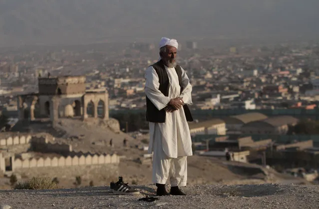 Abdul Latif, 57, an Afghan man, prays on Nadir Khan hill in Kabul, Afghanistan, Thursday, October 31, 2013. The hill is known for the cemetery of the last Afghan king, Mohammad Zahir Shah, and his family. The building, left, in the background is an unknown tomb. (Photo by Rahmat Gul/AP Photo)