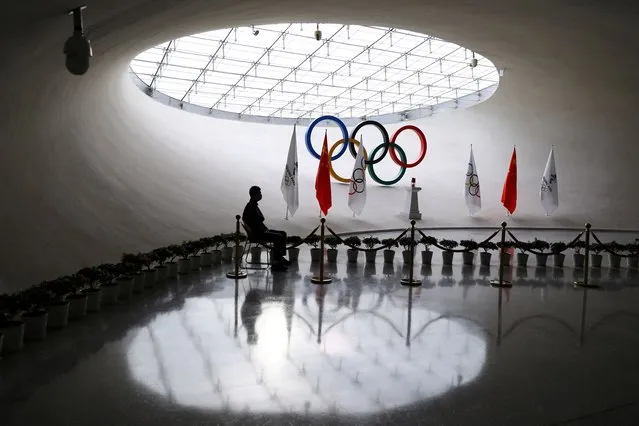 A staff member sits near a safety lantern carrying the Olympic flame of the Beijing 2022 Winter Olympics that is displayed on a podium inside the Olympic Tower, in Beijing, China on December 10, 2021. (Photo by Tingshu Wang/Reuters)