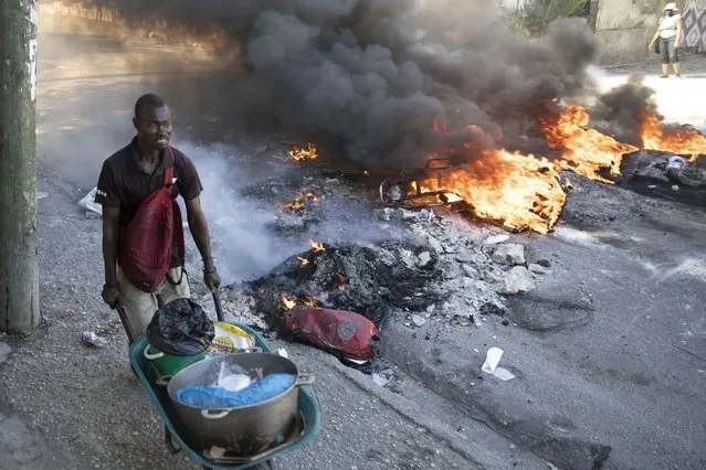A street vendor pushes his wheelbarrow past burning barricades set up by protesters in reaction to rising fuel prices, in Port-au-Prince, Haiti, Friday, December 10, 2021. (Photo by Joseph Odelyn/AP Photo)