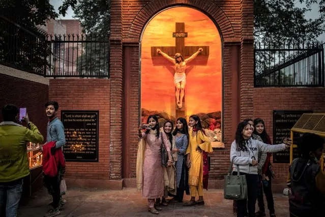 Indians take selfies in front of statue of Jesus Christ outside the gate of Sacred Heart Cathedral which is closed to general public due to COVID-19 restrictions on the eve of Christmas in New Delhi, India, Friday, December 24, 2021. (Photo by Altaf Qadri/AP Photo)