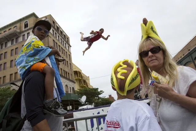 A man leaps on a trampoline behind attendees before the annual Fourth of July 2015 Nathan's Famous Hot Dog Eating Contest in Brooklyn, New York July 4, 2015. (Photo by Andrew Kelly/Reuters)