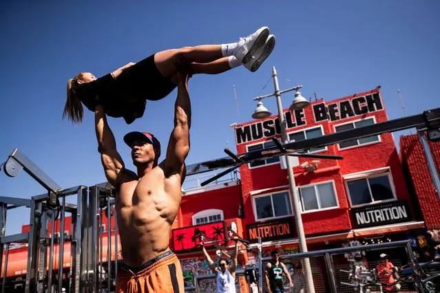 Bodybuilder Ike Catcher lifts a tourist in the air at Muscle Beach in Venice, California, USA, 14 March 2022. Muscle Beach reope​ned today after being closed because of the Covid-19 pandemic. (Photo by Etienne Laurent/EPA/EFE)