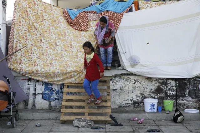 An Afghan girl get out her makeshift tent at the old international airport, which is used as a shelter for over 3,500 refugees and migrants, in southern Athens on Monday, May 30, 2016. The government has been moving migrants from makeshift camps into organized shelters and the Greek government said Monday they will continue to clear the Greek–Macedonian border area over the next few days. (Photo by Petros Giannakouris/AP Photo)
