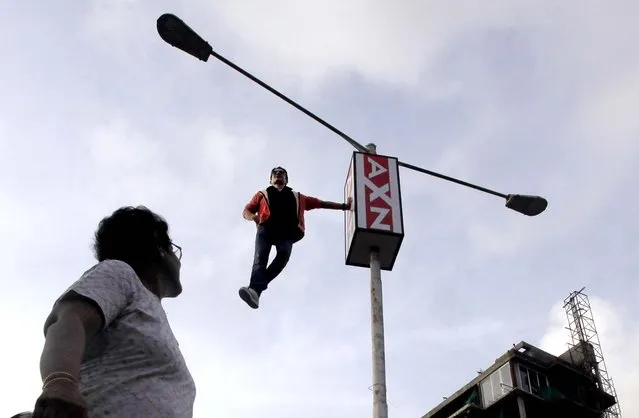 A woman watches as magician and illusionist Cyril Takayama performs on a roadside electric pole, in Mumbai, India on June 15, 2012