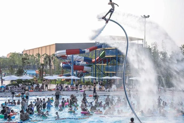 This photo taken on July 18, 2022 shows people watching a flyboard performance as they cool off in a pool to escape the hot weather at a water park in Huaian, in China's eastern Jiangsu province. (Photo by AFP Photo/China Stringer Network)