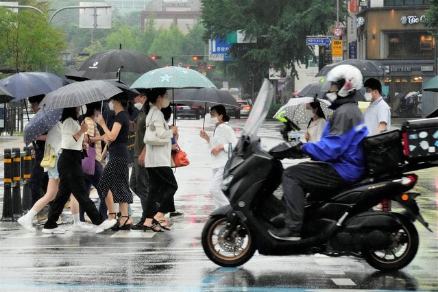 People wearing face masks cross a road in the rain near a subway station in Seoul, South Korea, Wednesday, July 13, 2022. (Photo by Ahn Young-joon/AP Photo)