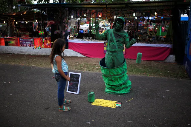 A girl observes a performer at the fair during the festivities of El Divino Salvador del Mundo (The Divine Savior of the World), patron saint of the capital city of San Salvador in San Salvador, El Salvador August 2, 2016. (Photo by Jose Cabezas/Reuters)