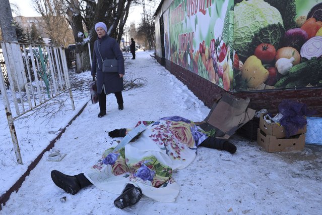 A woman walks past a body of a victim killed during the shelling that Russian officials in Donetsk said was conducted by Ukrainian forces, in Donetsk, Russian-controlled Donetsk region, eastern Ukraine in Donetsk, Ukraine, Sunday, January 21, 2024. Local officials say at least 18 people have been killed by shelling of a market in Russian-occupied Ukraine. The attack hit Tekstilshchik, a suburb of the city of Donetsk, on Sunday. Alexei Kulemzin, the city's Russian-installed mayor, said that the shells had been fired by the Ukrainian military. (Photo by Alexei Alexandrov/AP Photo)