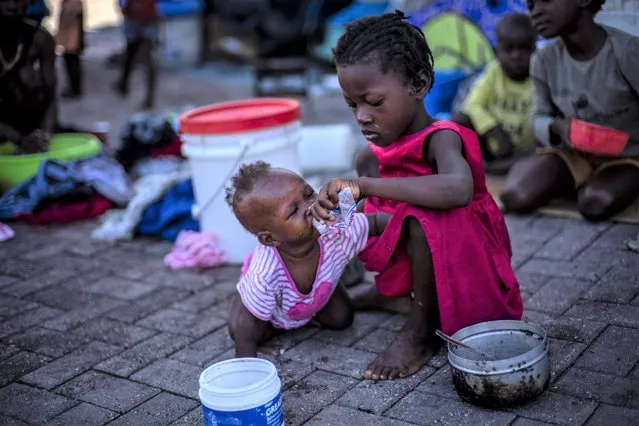 A girl helps a baby to drink water at the Hugo Chavez public square transformed into a refuge for families forced to leave their homes due to clashes between armed gangs, in Port-au-Prince, Haiti, Thursday, October 20, 2022. (Photo by Ramon Espinosa/AP Photo)