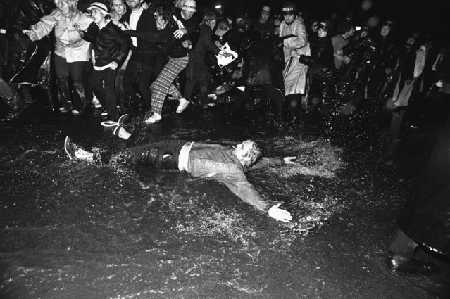 A picketers throws himself to the ground in a puddle in Boston as police try to keep others from preventing delivery trucks from leaving the Boston Globe plant with Sunday papers, September 21, 1974. A policeman was injured when one of the trucks tried to run the line. (Photo by Peter Bregg/AP Photo)