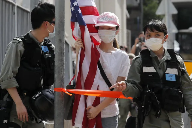 A protester carrying an American flag as she is stopped by riot police during a protest outside the U.S. Consulate in Hong Kong, Saturday, July 4, 2020 to mark the American Independence Day or “the Fourth of July”. China's government and pro-Beijing activists in Hong Kong are condemning what they call foreign meddling in the territory's affairs, as countries move to offer Hong Kongers refuge and impose sanctions on China over a new security law. (Photo by Kin Cheung/AP Photo)