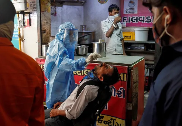 A healthcare worker wearing protective gear takes a swab sample from a man for a rapid antigen test, amidst the coronavirus disease (COVID-19) outbreak, outside a tea stall at a bus terminal in Ahmedabad, India, July 15, 2020. (Photo by Amit Dave/Reuters)