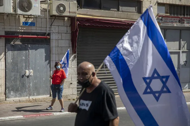 Supporters of Prime Minister Benjamin Netanyahu wave flags outside the district court in Jerusalem, Sunday, July 19, 2020. The corruption trial of Netanyahu has resumed following a two-month hiatus. (Photo by Ariel Schalit/AP Photo)