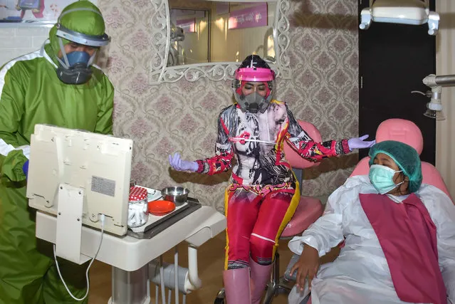 This picture taken on July 27, 2020, shows dentist Nina Agustin (C) and her assistant (L) preparing to examine their patient by wearing figured Personal Protective Equipments (PPE), in addition to attract patients' attention as well as a protection measures amid a COVID-19 coronavirus pandemic, at a clinic, in Malang, East Java province. (Photo by Aman Rochman/AFP Photo)