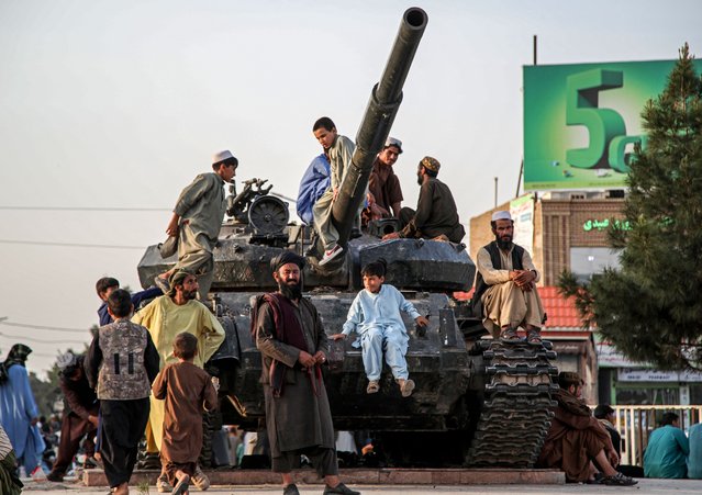 Afghan men and children sit over the remains of a Soviet-era tank at a square in Herat on April 16, 2025. (Photo by Mohsen Karimi/AFP Photo)