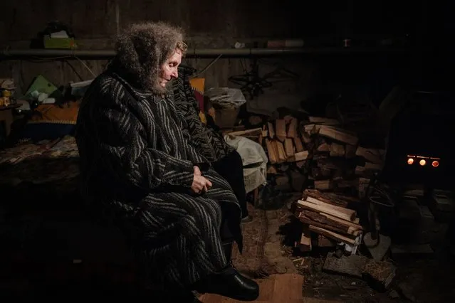 Lyubov Stepanova, 71, who lives in the basement of her apartment with about twenty other people, looks at a stove, as the sounds and vibrations of shelling continue in the frontline city of Avdiivka on February 8, 2023, amid the Russian invasion of Ukraine. (Photo by Yasuyoshi Chiba/AFP Photo)