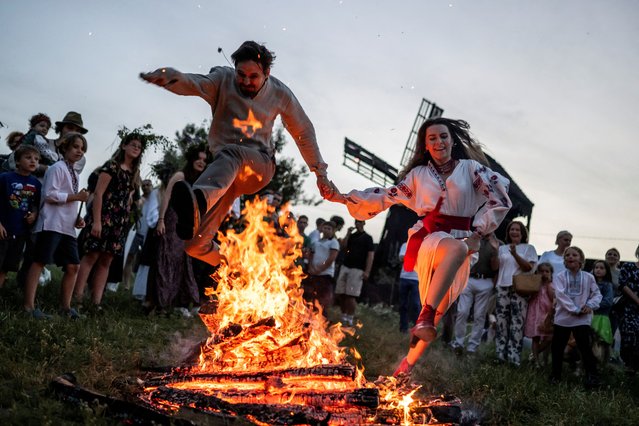 People jump over a campfire during a celebration on the traditional Ivana Kupala (Ivan the Bather) holiday, the ancient tradition, originating from pagan times, is marked with grand overnight festivities during which people sing and dance around campfires, believing it will purge them of their sins and make them healthier, amid Russia's attack on Ukraine, in the village of Vytachiv in Kyiv region, Ukraine on June 22, 2024. (Photo by Viacheslav Ratynskyi/Reuters)