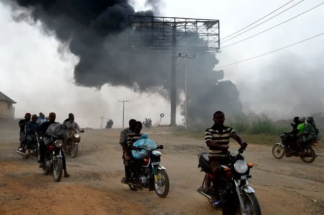 Taxi motorcyclists, popularly called Okada, drive past a tanker laden with petrol that is on fire after it fell over and spilt the contents across the Lagos-Ibadan expressway in Magboro, Ogun State, on December 2, 2020. Economic activities was grounded as traffic was brought to a halt on the Lagos -Ibadan expressway, the busiest inter-state route in Nigeria, after a petrol tanker exploded on the Magboro section after spilling the content across highway. (Photo by Pius Utomi Ekpei/AFP Photo)