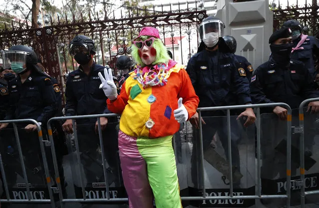 A pro-democracy protester wearing a clown clothing raises a three-finger salute, a symbol of resistance, in front of riot police at Police Headquarter in Bangkok, Thailand, Tuesday, February 23, 2021. (Photo by Sakchai Lalit/AP Photo)