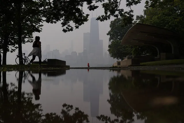 A person walks along the shore of Lake Michigan as the downtown skyline is blanketed in haze from Canadian wildfires Tuesday, June 27, 2023, in Chicago. (Photo by Kiichiro Sato/AP Photo)
