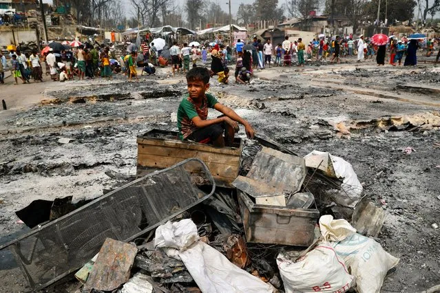 A Rohingya refugee boy sits on a stack of burned material after a massive fire broke out and destroyed thousands of shelters in a Rohingya refugee camp in Cox's Bazar, Bangladesh, March 24, 2021. (Photo by Mohammad Ponir Hossain/Reuters)