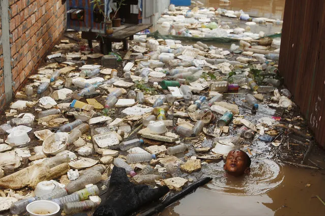 A boy swims near floating trash during flood season in the floating village on the Mekong river bank on the outskirts of Phnom Penh, Cambodia, Saturday, August 11, 2018. (Photo by Heng Sinith/AP Photo)