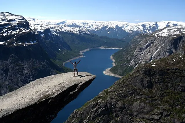 A man poses for a photo on Trolltunga ('Troll tongue') rock formation in Ullensvang Municipality, Vestland county, Norway, on June 10, 2023. The cliff of Trolltunga, popular with hikers and tourists, juts horizontally out from the mountain about 700 metres above lake Ringedalsvatnet. (Photo by Sergei Gapon/Anadolu Agency via Getty Images)