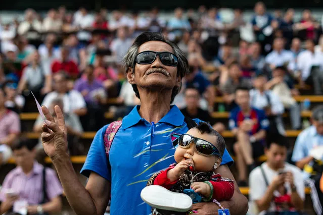 A man holds a baby doll during the season opening horse race at the Sha Tin Racecourse of the Hong Kong Jockey Club in Hong Kong on September 2, 2018. (Photo by Philip Fong/AFP Photo)