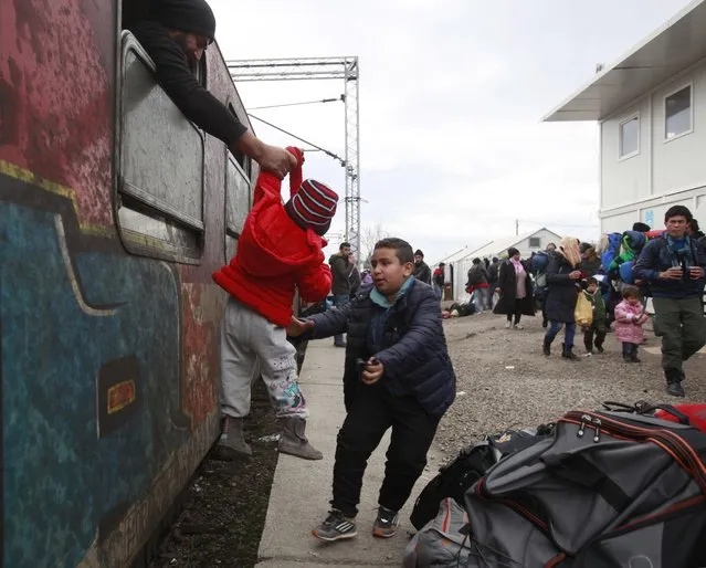 A refugee passes a baby from a train window to a boy, upon their arrival at the transit center for refugees near northern Macedonian village of Tabanovce, before continuing their journey to Serbia, Thursday, February 4, 2016. Macedonia has lifted restrictions on the entry of refugees from the Greek border after Macedonian taxi drivers ended a five-day protest that had closed a key railway line, slowing migrant flows to Serbia. (Photo by Boris Grdanoski/AP Photo)