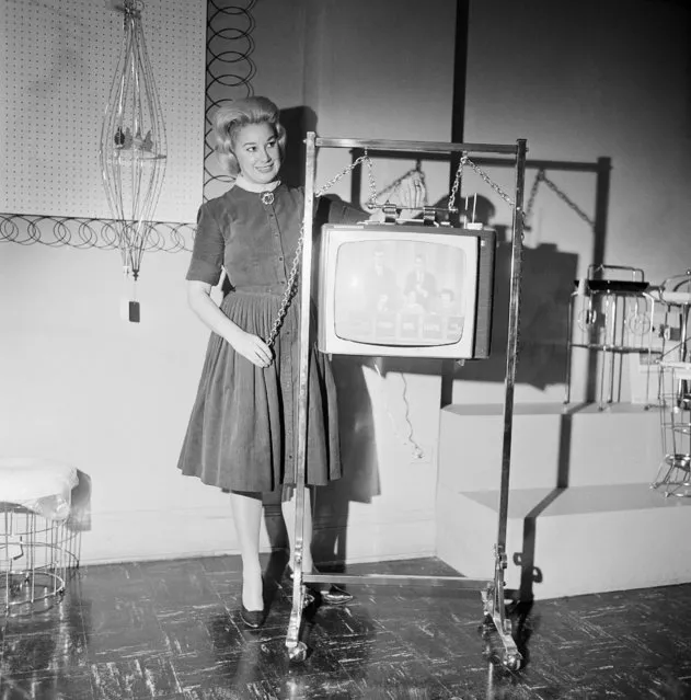 A portable television set can be raised or lowered to any height with this new stand, demonstrated by Carol Smith at the China Glass and Gift Market in Chicago, Ill., February 6, 1963. The stand, designed to hold a 19-inch TV set, is brass plated and lacquered, with chains and hooks to carry the set. (Photo by Edward Kitch/AP Photo)