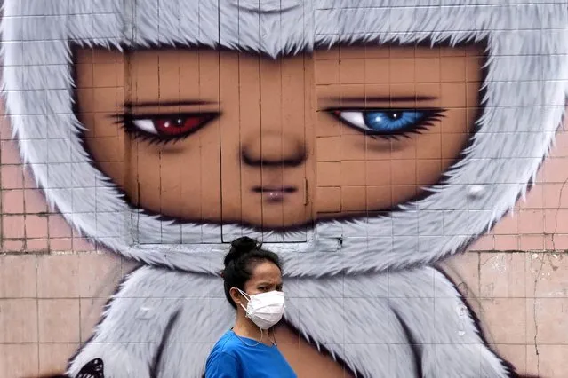 A woman wearing a face mask to help curb the spread the coronavirus walks past wall art in Bangkok, Thailand, Tuesday, July 20, 2021. (Photo by Sakchai Lalit/AP Photo)