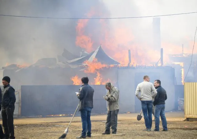 People watch burning houses in the village of Smolenka near Chita on Monday, April 13, 2015. (Photo by Evgeny Yepanchintsev/AP Photo)