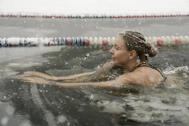 A young woman swims in ice water celebrating opening of the 65th winter swimming season of the Moscow Walrus Club in Serebryany Bor during heavy snowfall in Moscow, Russia, Sunday, December 3, 2023. A record snowfall has hit Russia's capital bringing an additional 10 cm to already high levels of snow and causing disruption at the capital's airports and on roads. (Photo by Pelagia Tikhonova/Moscow News Agency via AP Photo)