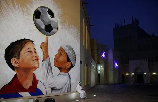 A man sits beside a football mural on the walls of Katara Cultural Village ahead of the FIFA World Cup in Doha, Qtar on November 9, 2022. (Photo by John Sibley/Reuters)