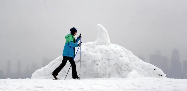 Gina Nakamura skis past a nearly life-size snow sculpture of an orca whale as downtown is just visible in a light snow Monday, February 11, 2019, in Seattle. Schools and universities closed across Washington state and the Legislature cancelled all hearings as the Northwest dealt with snow and ice and prepared for more as a series of winter storms socked the region. (Photo by Elaine Thompson/AP Photo)
