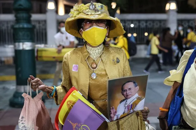 A royalist supporter holds a portrait of the late king late king Bhumibol Adulyadej while waiting for the motorcade of Thailand's King Maha Vajiralongkorn to pass in Bangkok on October 13, 2021, as the royals head to take part in a merit-making ceremony on the fifth anniversary of the passing of his father the late king. (Photo by Jack Taylor/AFP Photo)