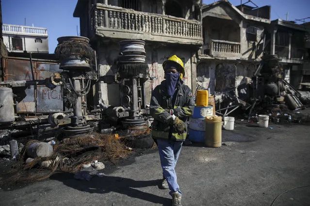 A firefighter stands next to the remains of a truck that was carrying gasoline and overturned in Cap-Hatien, Haiti, Tuesday, December 14, 2021. The truck exploded, engulfing cars and homes in flames, killing more than 50 people and injuring dozens of others. (Photo by Joseph Odelyn/AP Photo)