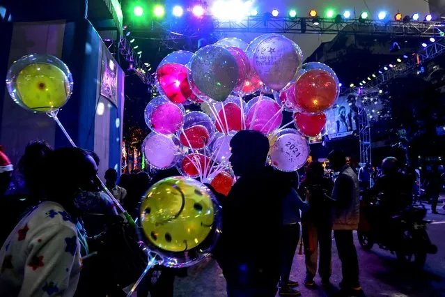 A vendor sells balloons on a decorated street on the Christmas Eve in Kolkata, India, Friday, December 24, 2021. (Photo by Bikas Das/AP Photo)