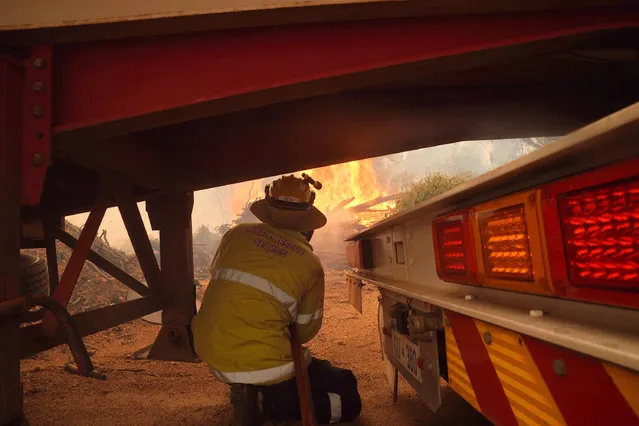 In this photo provided by Department of Fire and Emergency Services, a firefighter shelters under a truck and trailer as he works at a fire near Wooroloo, northeast of Perth, Australia, Tuesday, February. 2, 2021. An out-of-control wildfire burning northeast of the Australian west coast city of Perth has destroyed dozens of homes and was threatening more. (Photo by Evan Collis/DFES via AP Photo)