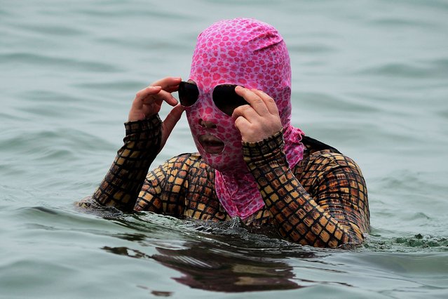 This photo taken on June 17, 2024 shows a woman wearing a facekini cooling off by a beach in Qingdao, in eastern China's Shandong province. (Photo by AFP Photo/China Stringer Network)