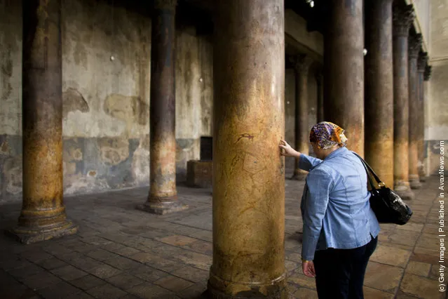 A woman places her fingers into the crucifix-shaped holes in one of the ancient columns in the Church of the Nativity