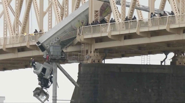 Louisville emergency crews rescue the driver of semitruck that is dangling off the Clark Memorial Bridge over the Ohio River on Friday, March 1, 2024 in Louisville, Ky.  The driver was pulled to safety by firefighters following the  three-vehicle crash on the bridge connecting Louisville, Kentucky to southern Indiana. (Photo by WDRB via AP Photo)