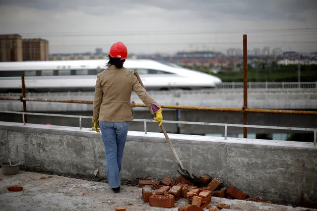 A construction worker watches a train pass on the high-speed railway line between Shanghai and Hangzhou on the outskirts of Shanghai Tuesday, October 26, 2010. (Photo by Carlos Barria/Reuters)