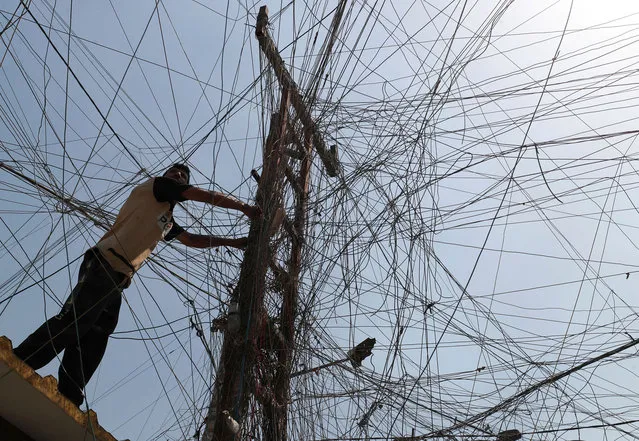 An Iraqi man connects overhead cables providing generator electricity to homes and businesses who can afford it in Sadr City, east of the capital Baghdad, on July 2, 2021, amid power outages and soaring temperatures. Anger has mounted among Iraq's 40-million population, with corrupt politicians at the centre of a blame game for its poor services and dilapidated infrastructure. Four southern provinces have been without electricity since June 29, including Basra – home to Iraq's main port– and sizzling temperatures have been compounded by high levels of humidity. (Photo by Ahmad Al-Rubaye/AFP Photo)