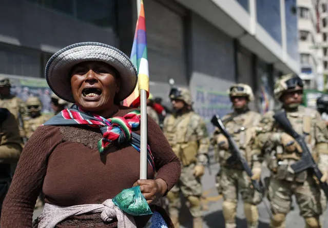 A backer of former President Evo Morales holds a Wiphala flag in front of soldiers blocking a street in downtown La Paz, Bolivia, Friday, November 15, 2019. (Photo by Natacha Pisarenko/AP Photo)