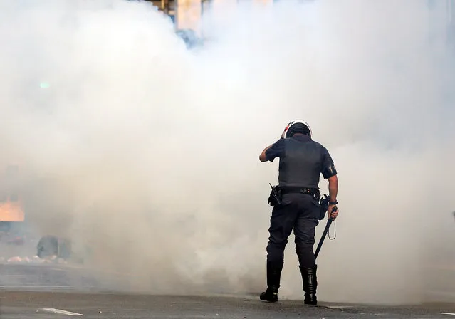 A police officer protects himself from tear gas during a Brazil's Homeless Workers' Movement (MTST) protest against Brazil's interim President Michel Temer and in support of suspended President Dilma Rousseff in Sao Paulo, Brazil, June 1, 2016. (Photo by Paulo Whitaker/Reuters)