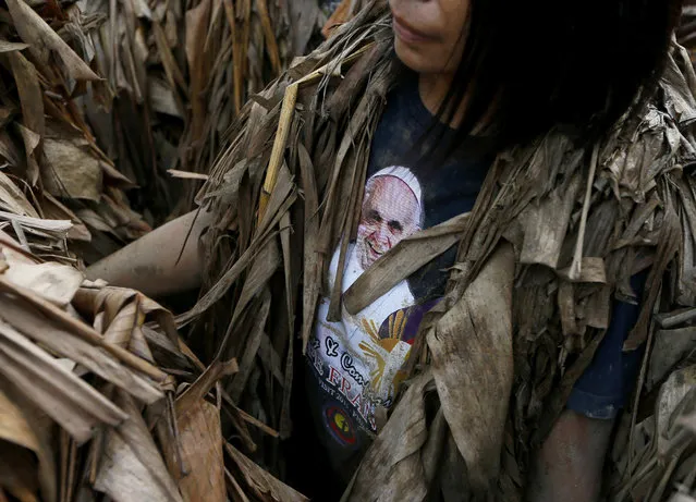 A villager, donning cape mostly of dried banana leaves and covered in mud, wears a t-shirt printed with Pope Francis as she attends a mass in a bizarre annual ritual to venerate their patron saint, John the Baptist, Friday, June 24, 2016 at Bibiclat, Aliaga township, Nueva Ecija province in northern Philippines. (Photo by Bullit Marquez/AP Photo)