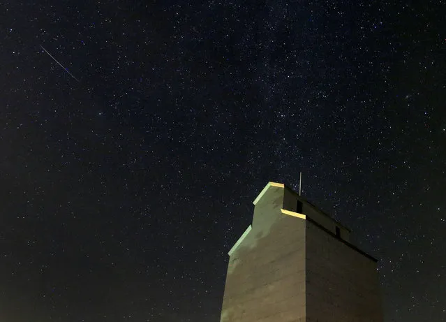 In this photo taken with long exposure, a meteor streaks across the sky behind a grain elevator during the annual Perseid meteor shower Thursday, August 13, 2015, in Baxter, Iowa. (Photo by Charlie Riedel/AP Photo)