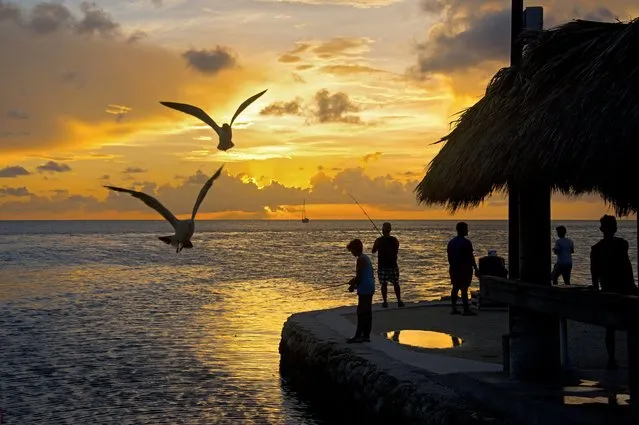 In this Friday, June 25, 2016, photo provided by the Florida Keys News Bureau, youngsters fish off a Fiesta Key, Fla., seawall at sunset while seagulls hover awaiting for fish scraps tossed into the bay by an angler cleaning his catch. With the school year ended for most students, the Florida Keys is a popular family summer travel destination. (Photo by Andy Newman/Florida Keys News Bureau via AP Photo)